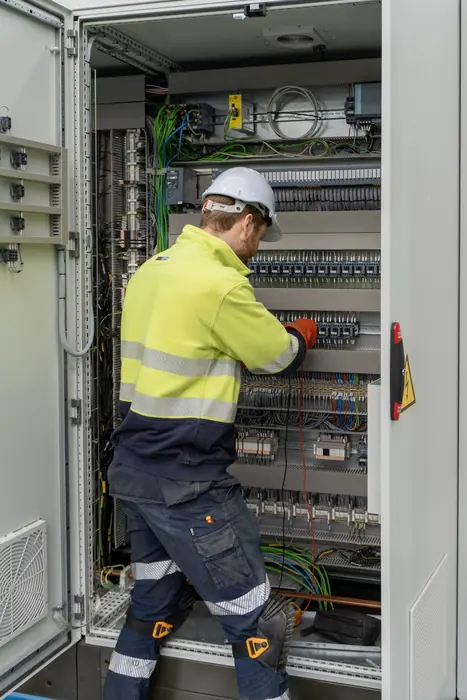 Industrial electrician working inside a control cabinet on site